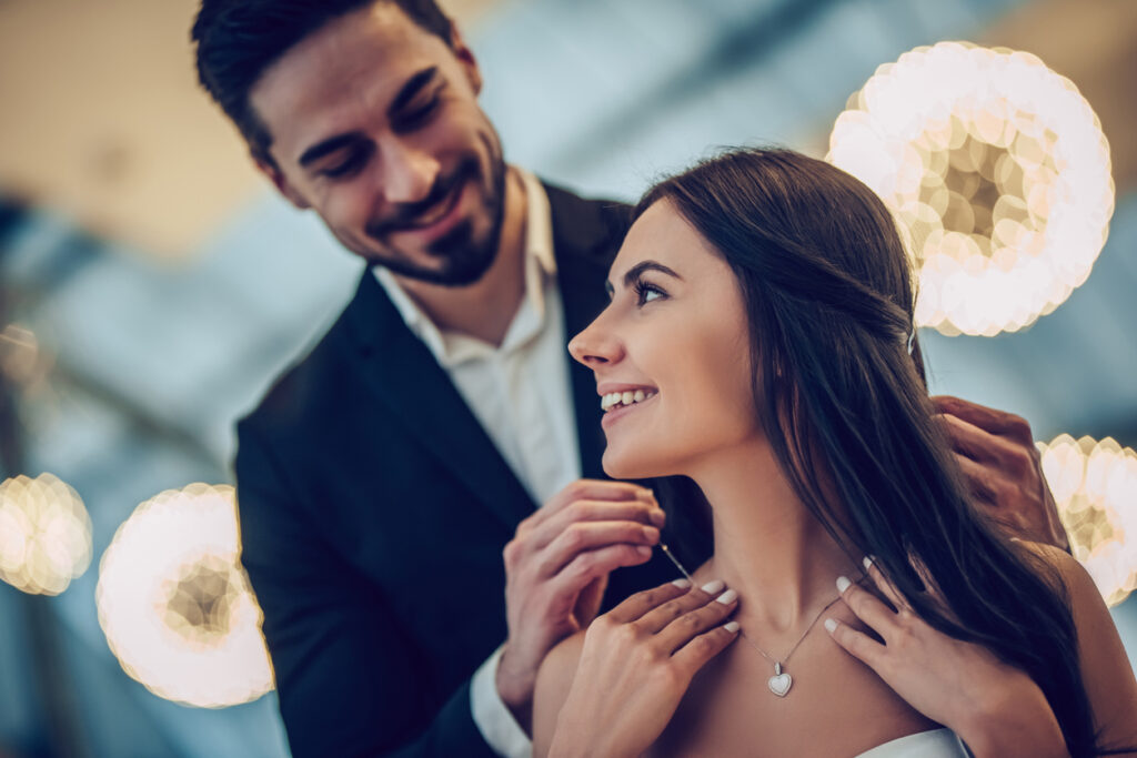 A young couple are having a romantic dinner. Man is giving the woman a beautiful necklace.