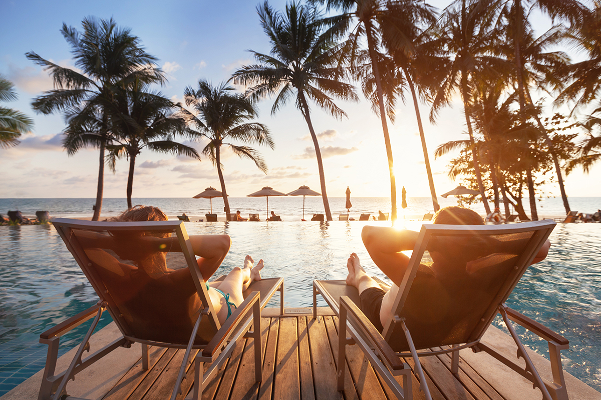 two people sitting in beach chairs at luxury tropical resort in front of sunset